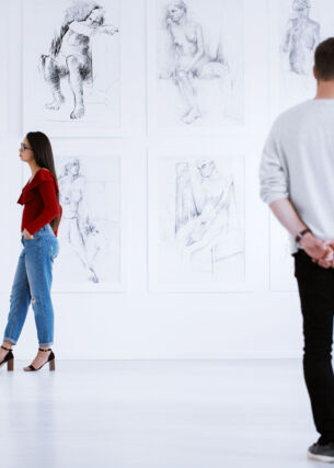 Zwei Personen schauen sich in einem weißen Ausstellungsraum Zeichnungen und Skulpturen an