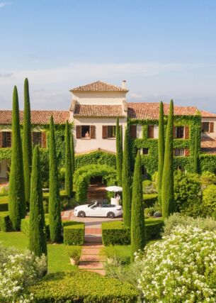 Ein begrüntes, luxuriöses Herrenhaus im französischen Stil, umgeben von einem Garten mit Zypressen