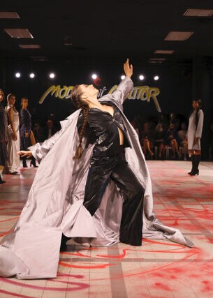 Eine Tänzerin mit weitem Mantel auf dem Catwalk umringt von stehenden Models