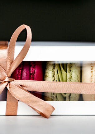 Eine Packung Macarons, dekoriert mit einem beigen Geschenkband