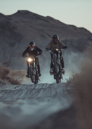 Zwei Motorradfahrer fahren in der Dämmerung durch eine Wüstenlandschaft