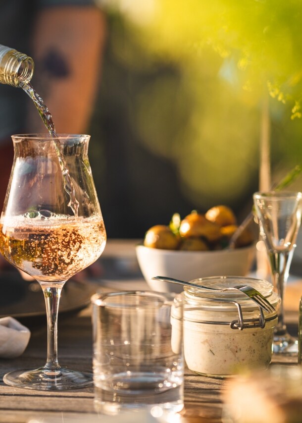 Ein Glas auf einem gedeckten Gartentisch, in das Rosé eingeschenkt wird