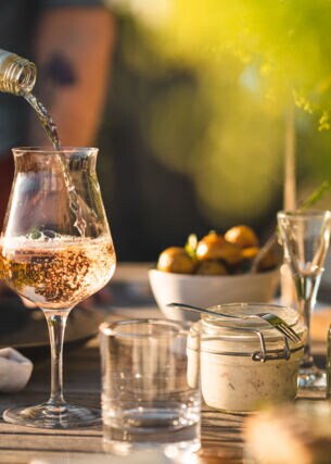 Ein Glas auf einem gedeckten Gartentisch, in das Rosé eingeschenkt wird