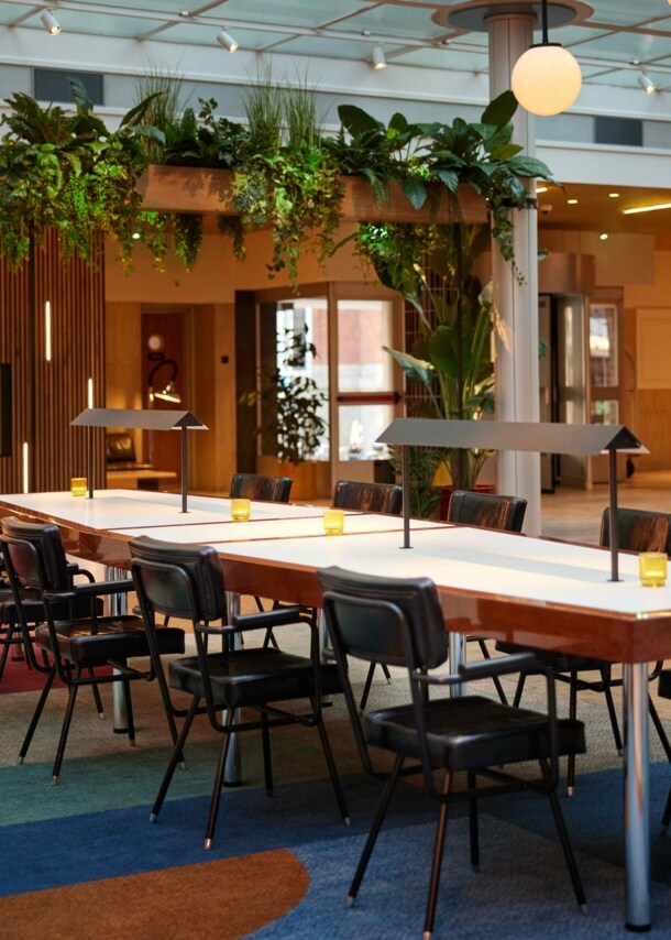 Langer Tisch mit Stühlen in einer Hotel-Lobby, im Hintergrund eine beleuchtete Bar