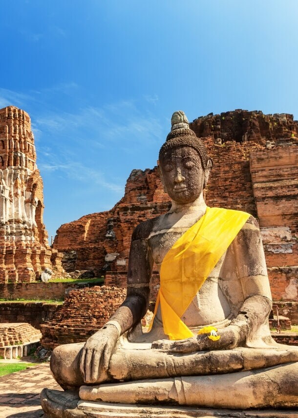Eine Buddhastatue vor Ruinen eines Tempels