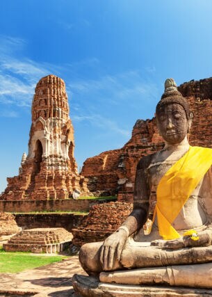 Eine Buddhastatue vor Ruinen eines Tempels