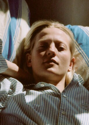 Porträt einer jungen Frau, die in einem gestreiften Pyjama auf gestreifter Bettwäsche im Sonnenlicht liegt