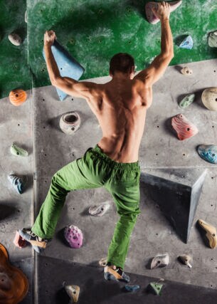 Ein Mann in grüner Hose und mit nacktem Oberkörper bouldert an einer Kletterwand
