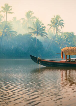 Ein traditionelles Hausboot bei Sonnenuntergang in den Backwaters im Palmenduschungel von Kerala