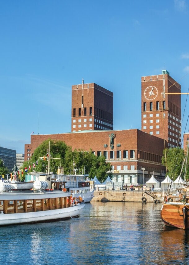 Blick auf das rote Rathaus von Oslo mit Backsteintürmen vom Wasser aus, im Vordergrund Segelboote
