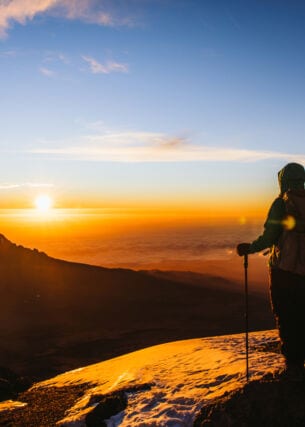 Eine Wanderin blickt vom Gipfel des Kilimandscharo in den Sonnenaufgang