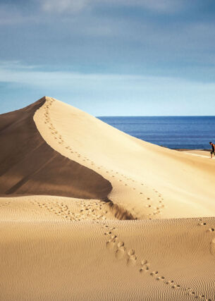 Zwei Personen wandern auf einer großen Sanddüne am Meer
