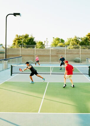 Vier Spieler bei einem Pickleball-Match auf einem Tennishartplatz unter freiem Himmel