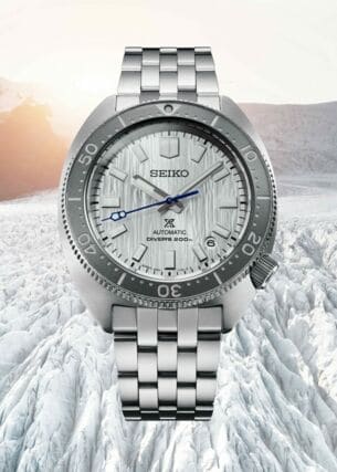 Uhr mit silbernem Armband und Ziffernblatt vor einer weißen, bergigen Schneelandschaft