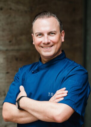 Lächelndes Porträt von Tim Raue in einer blauen Kochjacke