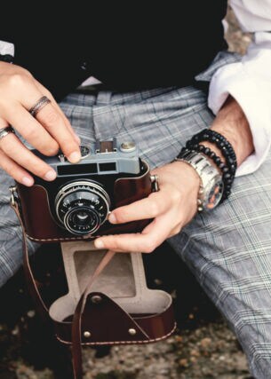 Eine Person sitzt auf einem Stein und hält eine analoge Kamera in den Händen