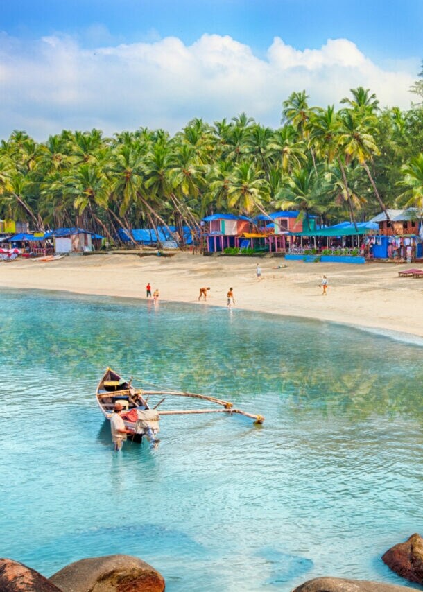 Strand mit bunten Holzhütten und Palmen, im Vordergrund Felsen
