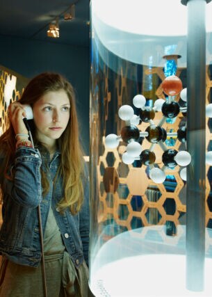 Eine junge Frau steht im Deutschen Technikmuseum in Berlin vor dem Modell eines Moleküls