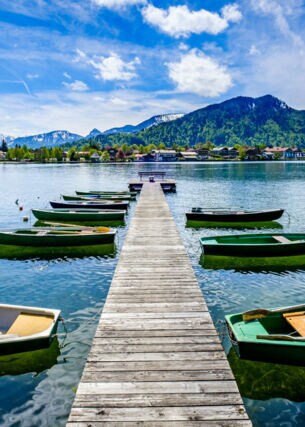 Ein Holzsteg mit kleinen Booten auf einem See, im Hintergrund Berge