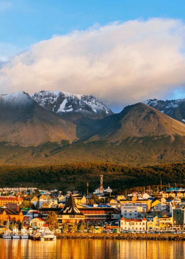 Stadtpanorama von Ushuaia am Wasser vor Bergkulisse im Sonnenuntergang