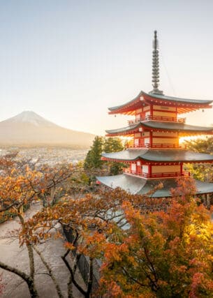Ein mehrstöckiger, japanischer Tempel mit roten Ornamenten, im Hintergrund eine Stadt am Fuße des Mount Fuji