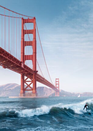 Ein Surfer auf einer Welle unter der roten Golden Gate Bridge