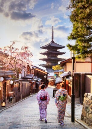 Zwei Frauen in bunten Kimonos laufen durch eine Gasse in der Altstadt von Kyoto auf einen Tempel zu