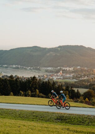 Zwei Radfahrer fahren auf dem Donauradweg mit Blick auf Berge