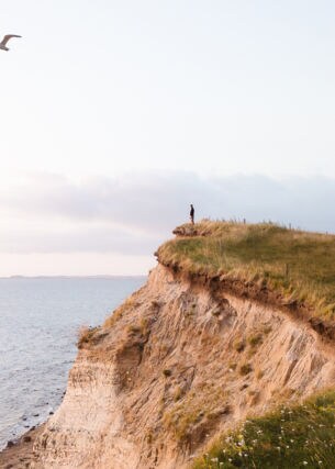 Eine Person steht auf einer Klippe und blickt aufs Meer