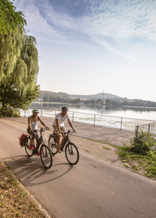 Ein Paar in Sommerkleidung fährt auf Fahrrädern auf einem Radweg entlang eines Flusses