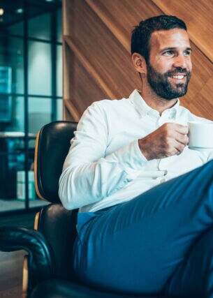 Ein Geschäftsmann sitzt entspannt mit einer Kaffeetasse in einem Sessel in einer Flughafen-Lounge