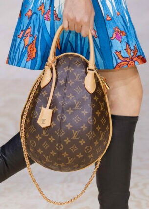 Nahaufnahme einer braunen, oval förmigen Lederhandtasche mit Louis Vuitton Monogramm-Muster in der Hand einer Frau in Minirock