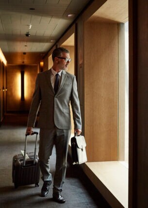 Ein Mann in Anzug zieht einen Businesstrolley über einen Hotelflur
