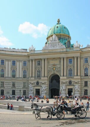 Personen und Pferdekutschen auf einem Platz vor der Wiener Hofburg