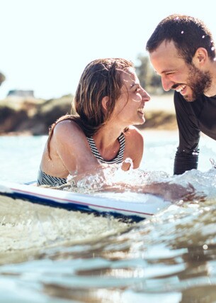 Ein lachendes Paar im Meer auf einem Surfboard