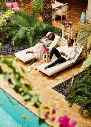 Aufsicht eines elegant gekleideten Paares auf Sonnenliegen an einem Pool auf der Terrasse eines Boutiquehotels.