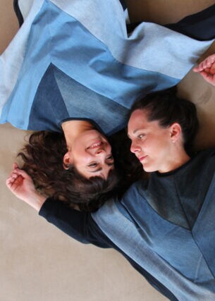 Aufsicht von zwei Frauen, die in blau gemusterten Sweatshirts kopfüber nebeneinander liegen