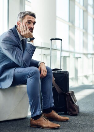 Mann in Anzug auf Sitzmöbel am Flughafen stützt den Kopf in seine Hände