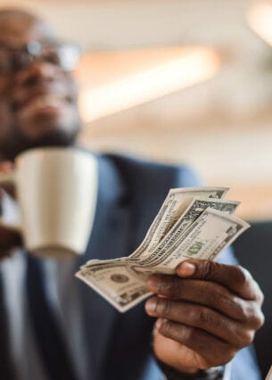 Nahaufnahme von US-Dollar-Scheinen in der Hand eines Geschäftsmannes beim Bezahlen eines Kaffees.