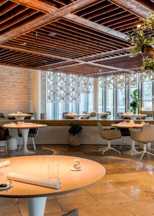 Modernes Restaurant mit runden Tischen und einem Olivenbaum in einem Rundbeet.