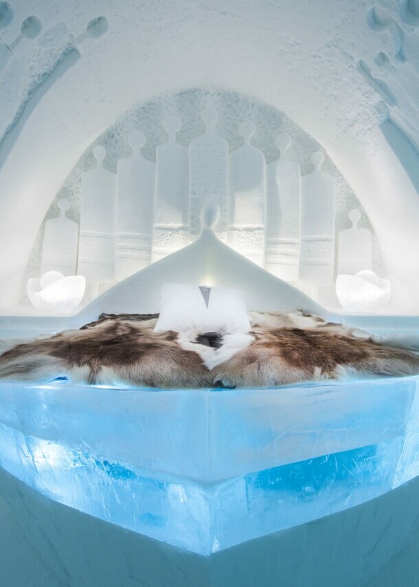 Innenansicht eines Zimmers in einem Eishotel mit Rentierfellen auf dem Bett.
