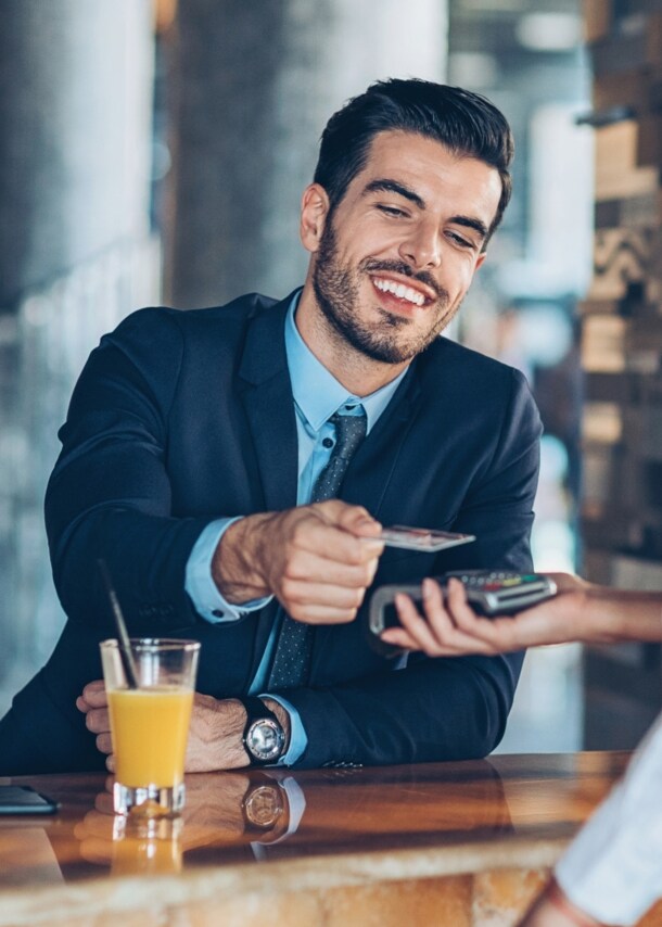 Ein junger Geschäftsmann bezahlt kontaktlos mit seiner Kreditkarte an einer Hotelbar.