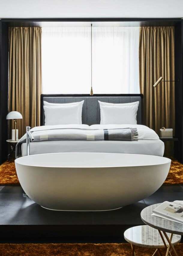 Moderne Hotelsuite mit einer freistehenden Badewanne vor einem Doppelbett.