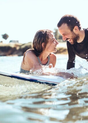 Ein lachendes Paar im Meer auf einem Surfboardon-Surfer