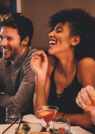 Eine Gruppe junger Menschen sitzt gut gelaunt mit Getränken an einem Tisch in einem Restaurant.