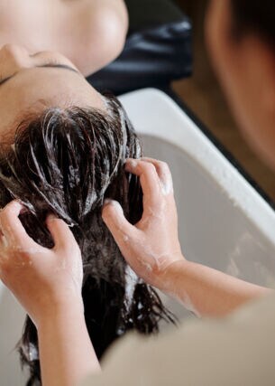 Die Haare einer liegenden Frau werden an einem Waschbecken von einer anderen Person gewaschen.