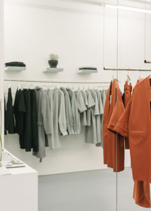 Puristische, elegante Kleidungsstücke, nach Farben sortiert, auf hängenden Kleiderstangen in einer Boutique.