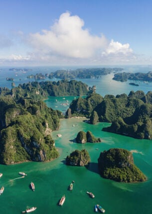 Aufnahme aus der Vogelperspektive von Booten und vielen kleinen von dichter Fauna bewachsenen Inseln in der vietnamesischen Halong-Bucht.
