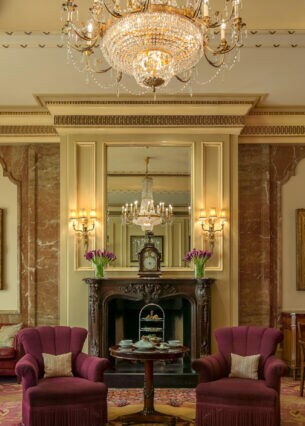 Edle, altehrwürdige Hotel Lobby Lounge mit Teppichboden, Goldverzierungen und roten Polstermöbeln unter einem Kronleuchter.