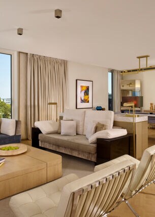 Eine modern und mit hellem Mobiliar eingerichtete Hotel-Suite mit großer Fensterfront.